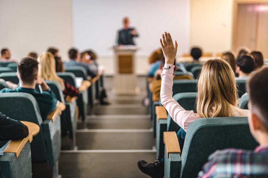 Student raising her hand in a lecture hall.